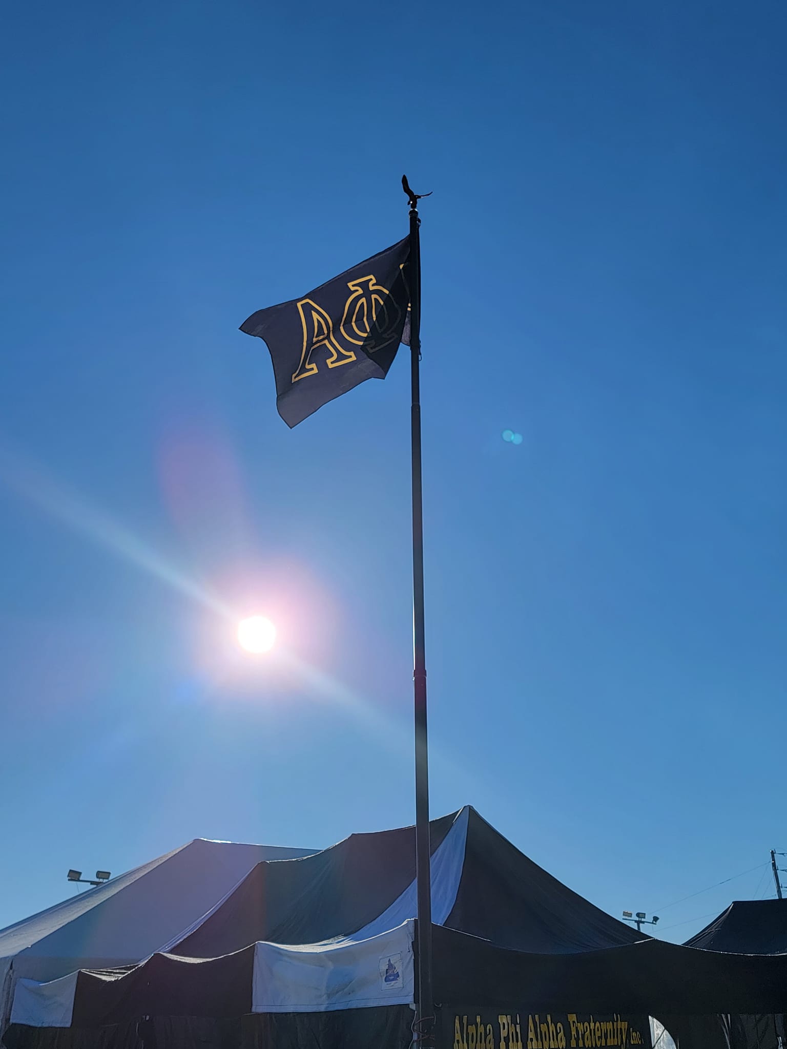 The Alpha Phi Alpha flag flying high above the chapter tents against a bright blue sky.