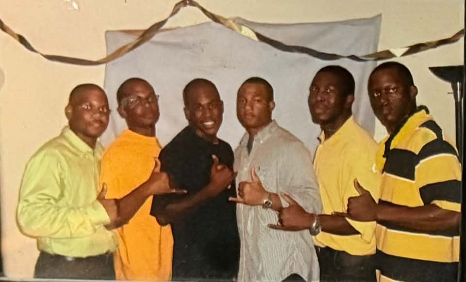 The Fall 2004 Dungeon Phamily line posed shoulder-to-shoulder in front of a draped backdrop with streamers, wearing casual shirts and each throwing the Alpha hand sign.