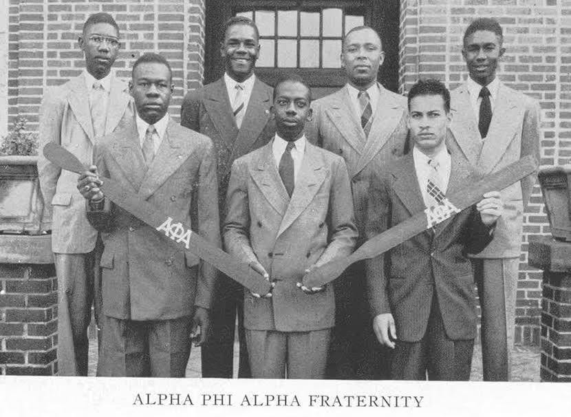 The founding brothers of the Gamma Zeta Chapter of Alpha Phi Alpha Fraternity in suits, holding fraternity canes, outside a brick building at Fort Valley State College.