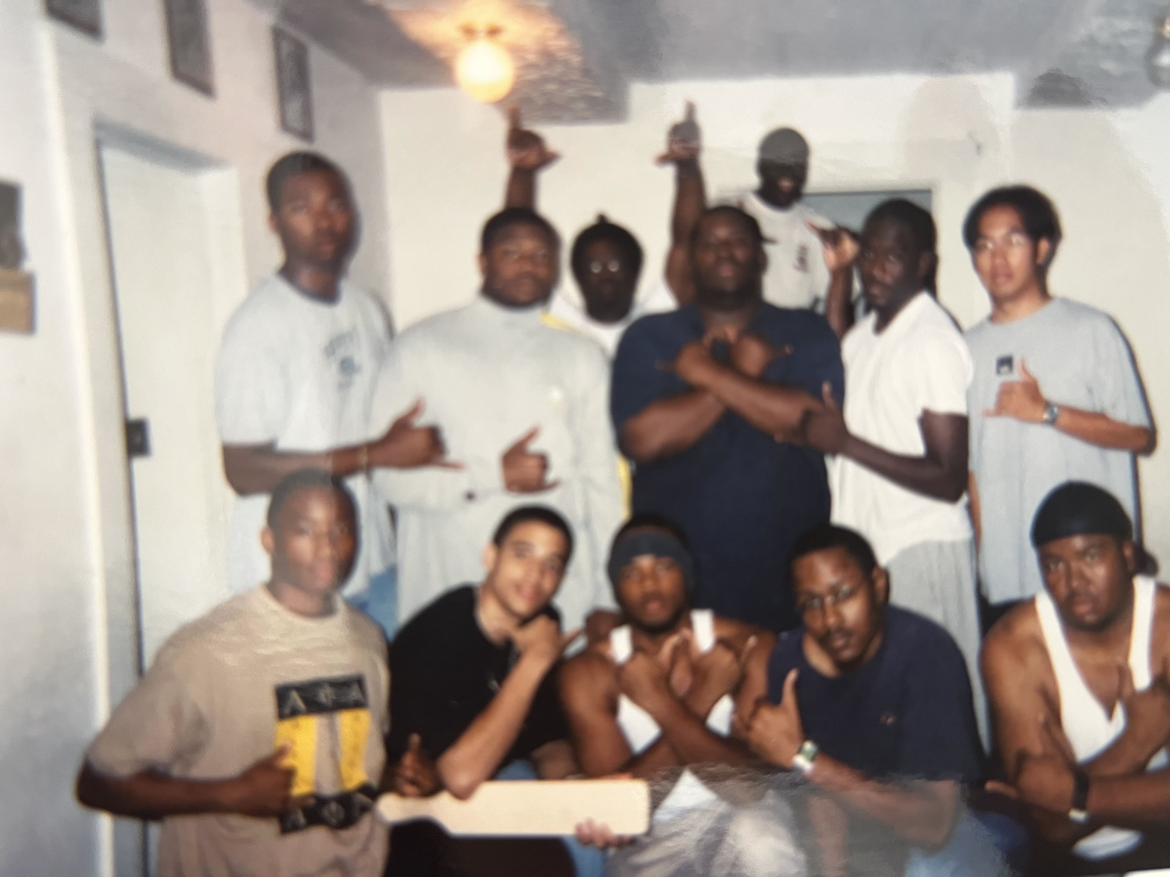 The Legends of the Fall line during their 1998 crossing era, gathered indoors with an Alpha Phi Alpha paddle, throwing the fraternity hand sign.
