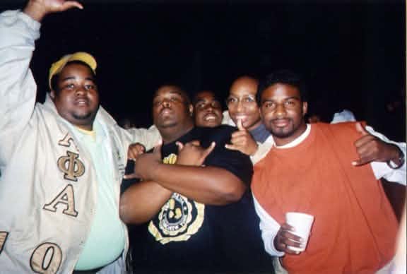The Fall 1999 Phi 2 K line at a night event, one brother in an Alpha Phi Alpha letterman jacket, throwing hand signs.